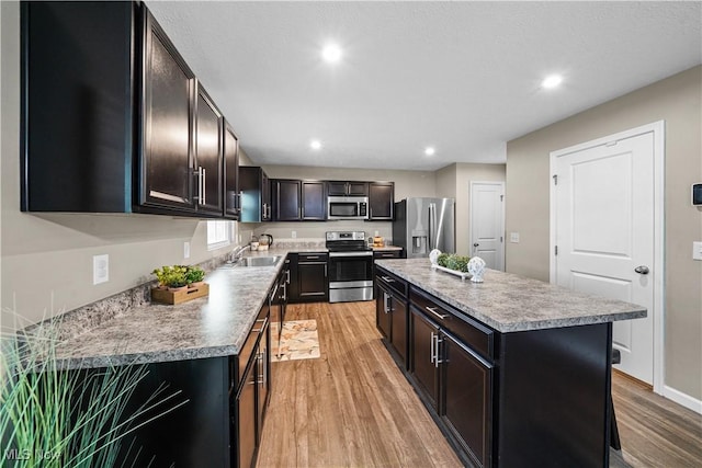 kitchen with a sink, light wood-type flooring, appliances with stainless steel finishes, and a center island