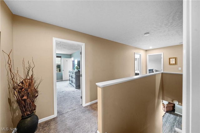 hall featuring carpet, an upstairs landing, baseboards, and a textured ceiling