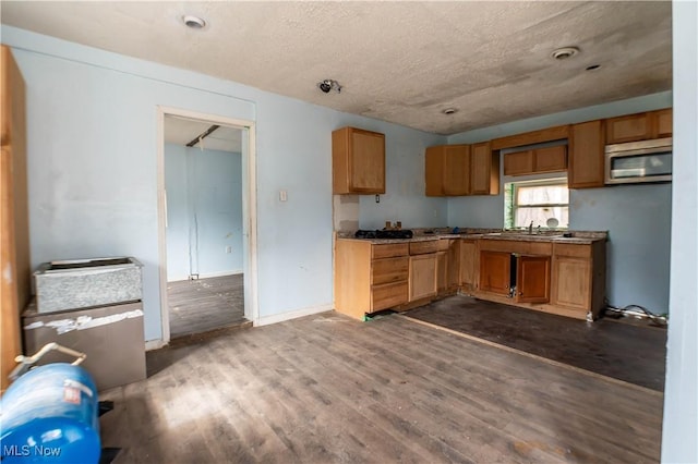 kitchen featuring dark wood-style flooring, brown cabinets, stainless steel microwave, a sink, and a textured ceiling