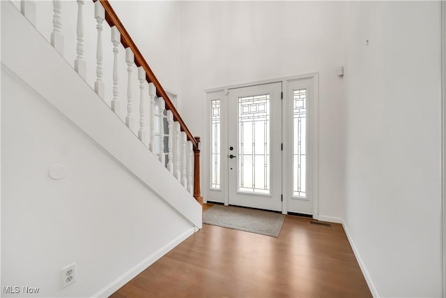 foyer entrance featuring a high ceiling, wood finished floors, visible vents, baseboards, and stairway