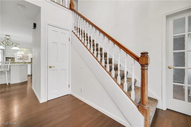 stairway featuring baseboards, a high ceiling, and wood finished floors