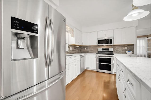 kitchen with stainless steel appliances, light wood-style floors, backsplash, and white cabinets