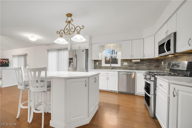 kitchen with a center island, stainless steel appliances, light countertops, backsplash, and white cabinetry