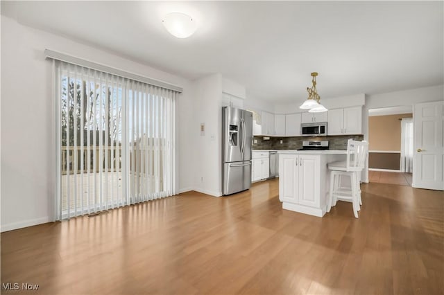 kitchen with white cabinets, a breakfast bar area, wood finished floors, stainless steel appliances, and backsplash