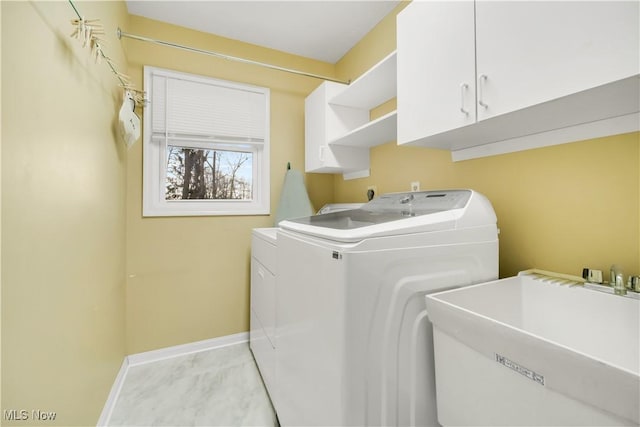 laundry area featuring washing machine and clothes dryer, a sink, cabinet space, and baseboards