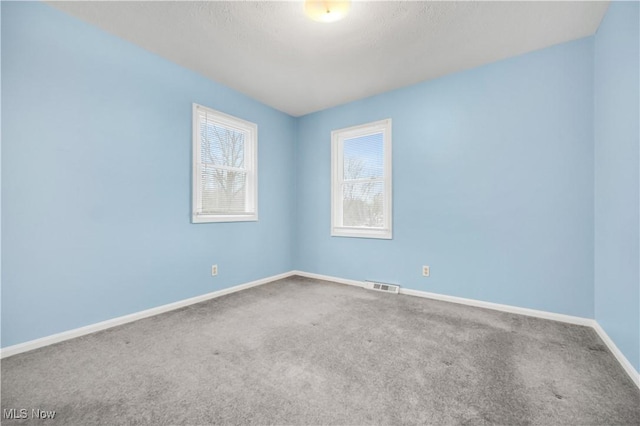 spare room featuring carpet, visible vents, and baseboards