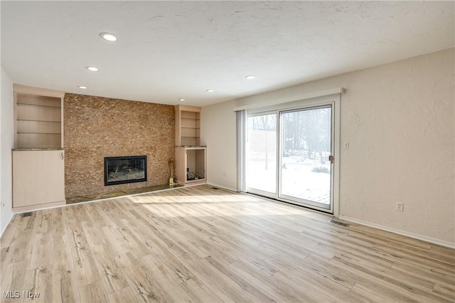 unfurnished living room featuring a large fireplace, built in shelves, baseboards, and wood finished floors