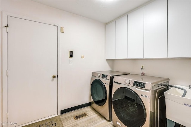 laundry area with cabinet space, visible vents, light wood-style flooring, washer and dryer, and a sink