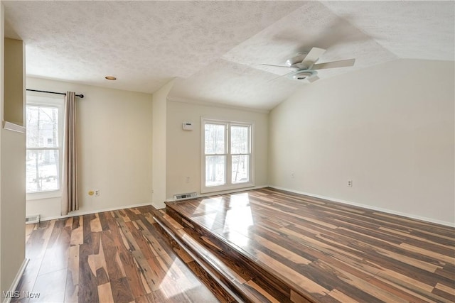 empty room with a wealth of natural light, wood finished floors, and visible vents