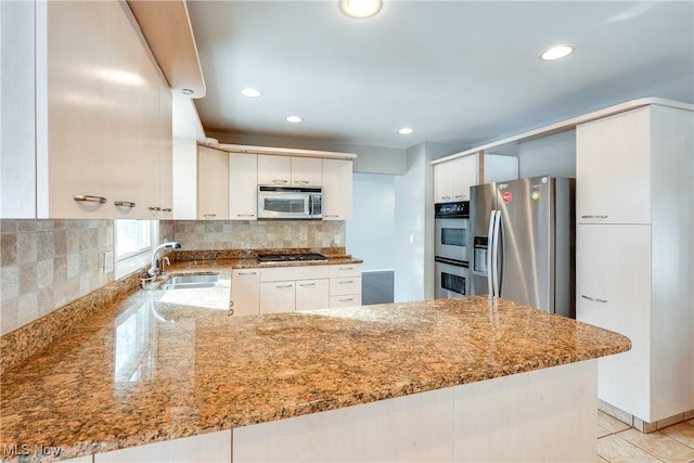 kitchen featuring light stone counters, stainless steel appliances, a sink, white cabinets, and decorative backsplash