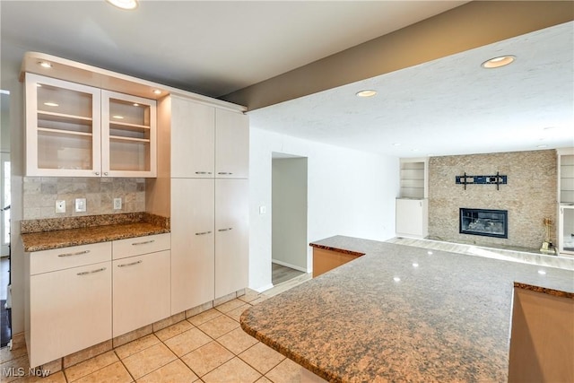 kitchen featuring glass insert cabinets, a large fireplace, dark stone countertops, and light tile patterned floors