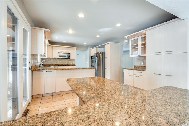 kitchen featuring light stone counters, visible vents, appliances with stainless steel finishes, tasteful backsplash, and glass insert cabinets