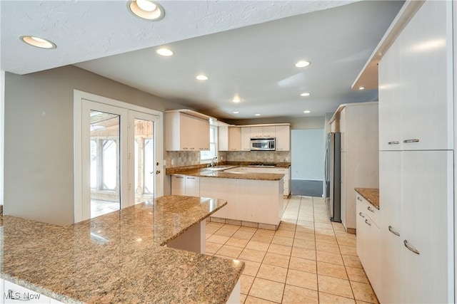 kitchen with light tile patterned floors, backsplash, appliances with stainless steel finishes, white cabinetry, and a sink