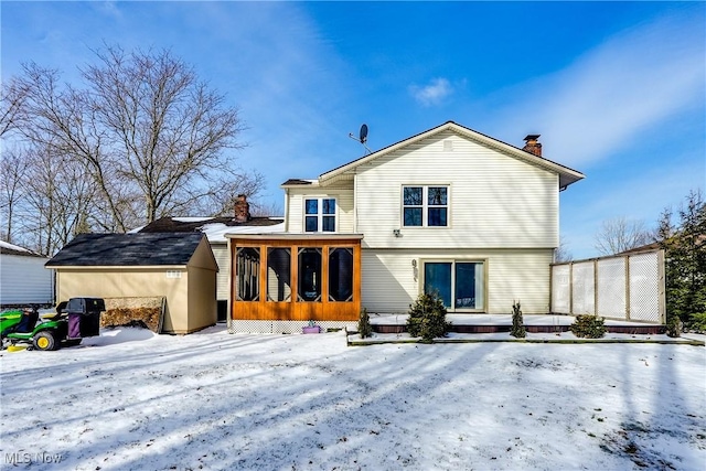 snow covered property featuring a chimney, an outdoor structure, and a sunroom