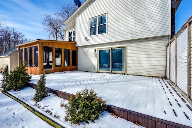 snow covered rear of property featuring a sunroom