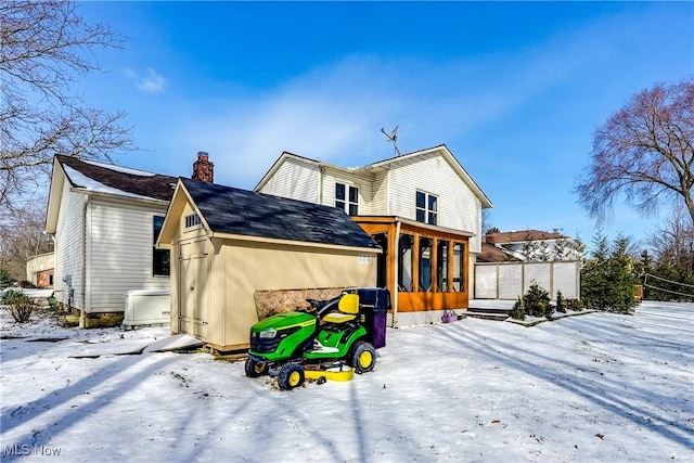 snow covered rear of property with a chimney and a sunroom