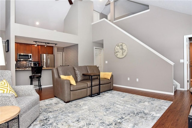 living area featuring high vaulted ceiling, dark wood finished floors, baseboards, and stairs