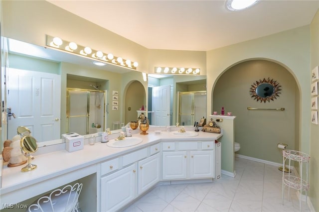 bathroom featuring double vanity, a sink, toilet, and a shower stall