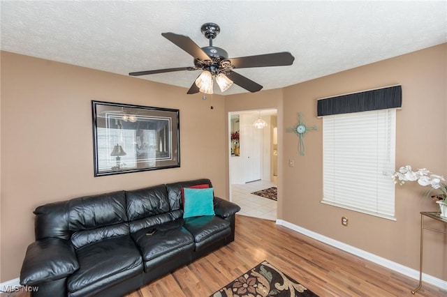 living room with baseboards, ceiling fan, a textured ceiling, and light wood finished floors