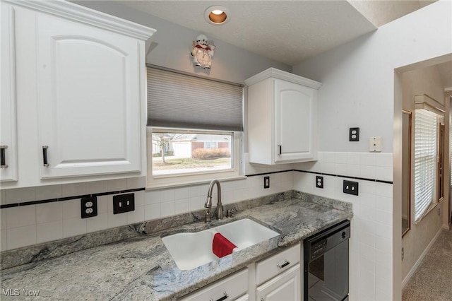 kitchen featuring light stone counters, a sink, white cabinetry, tile walls, and black dishwasher