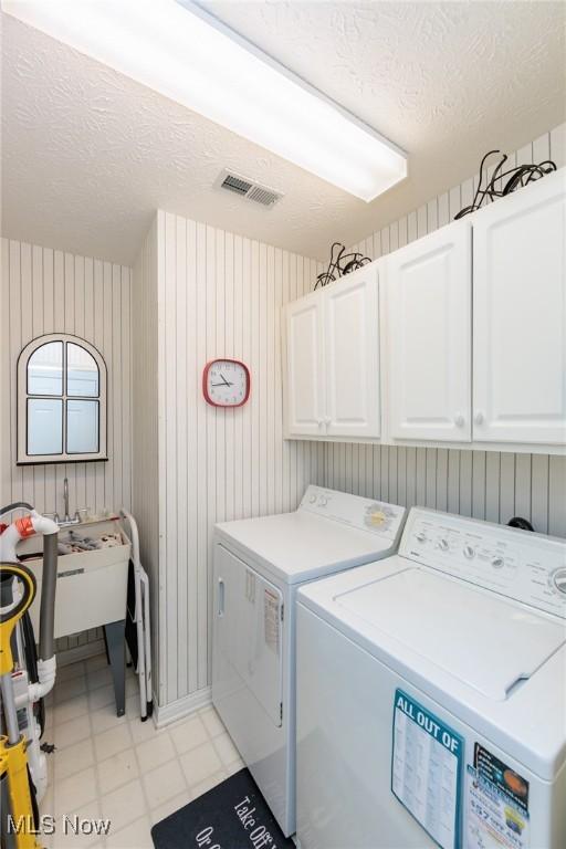 clothes washing area featuring a textured ceiling, visible vents, independent washer and dryer, cabinet space, and light floors