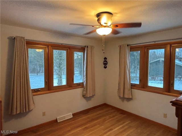 empty room featuring light wood-style flooring, a ceiling fan, visible vents, and baseboards