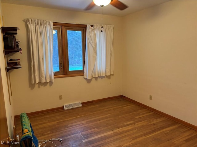 spare room featuring ceiling fan, wood finished floors, visible vents, and baseboards