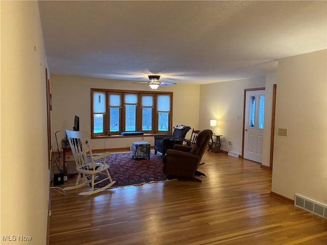 living area featuring ceiling fan, wood finished floors, visible vents, and baseboards