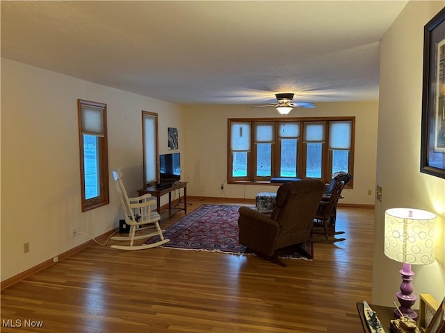 living area with wood finished floors, a ceiling fan, and baseboards