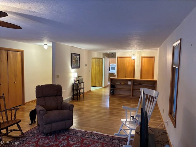 living room with a textured ceiling, baseboards, and wood finished floors