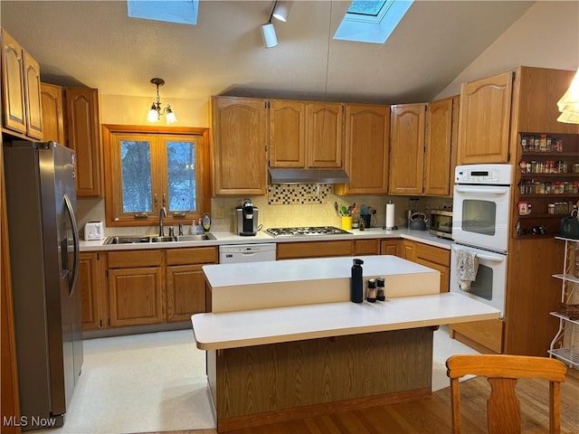 kitchen featuring stainless steel appliances, light countertops, a sink, vaulted ceiling with skylight, and under cabinet range hood