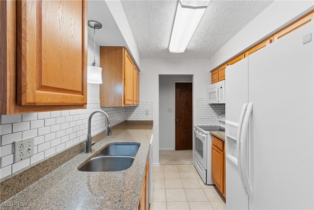 kitchen with white appliances, light tile patterned floors, decorative light fixtures, light stone countertops, and a sink