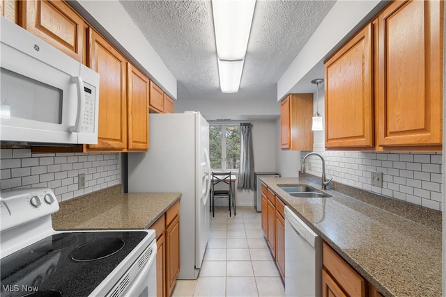 kitchen featuring light tile patterned floors, a textured ceiling, white appliances, a sink, and brown cabinets