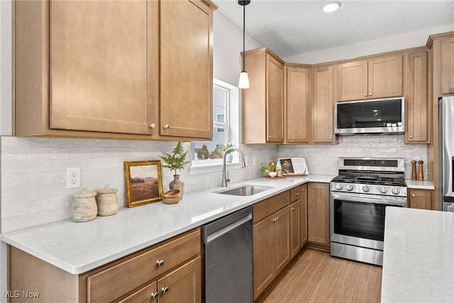 kitchen featuring a sink, hanging light fixtures, appliances with stainless steel finishes, backsplash, and light wood finished floors