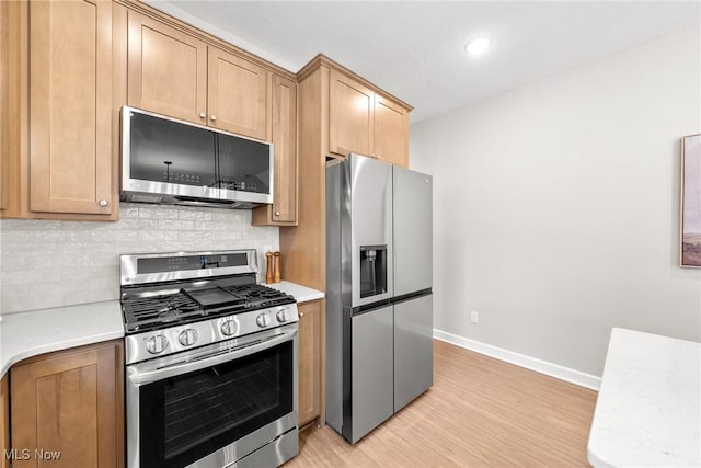 kitchen featuring light wood finished floors, tasteful backsplash, light countertops, appliances with stainless steel finishes, and baseboards