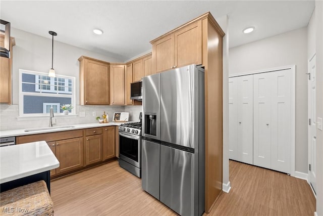 kitchen with appliances with stainless steel finishes, backsplash, light wood-type flooring, and a sink