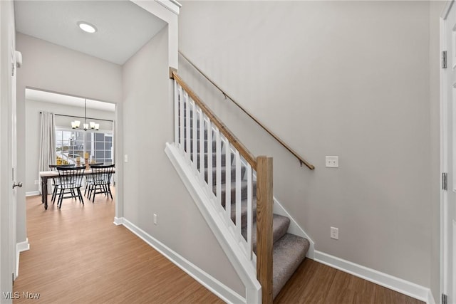 stairs with a notable chandelier, wood finished floors, and baseboards