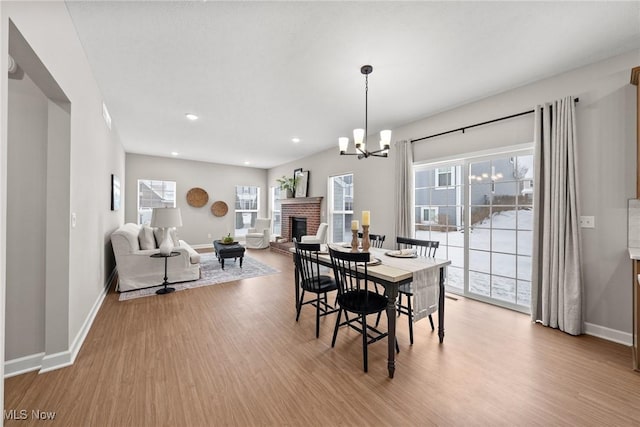 dining room featuring a brick fireplace, wood finished floors, an inviting chandelier, and baseboards