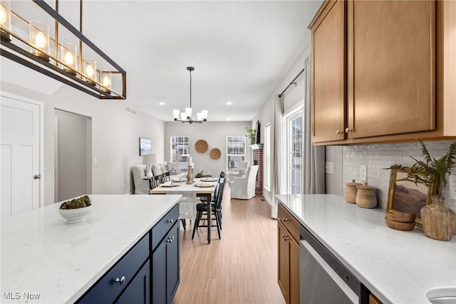 kitchen with light wood-style flooring, hanging light fixtures, stainless steel dishwasher, a chandelier, and backsplash