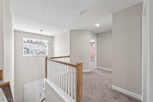 corridor featuring a textured ceiling, a notable chandelier, an upstairs landing, baseboards, and carpet