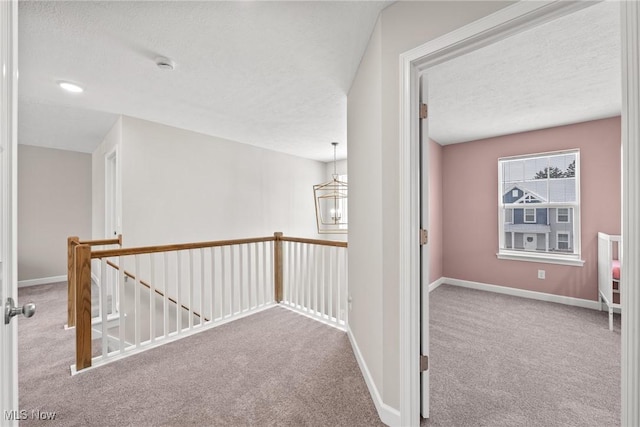 hallway featuring an upstairs landing, carpet, a textured ceiling, and baseboards