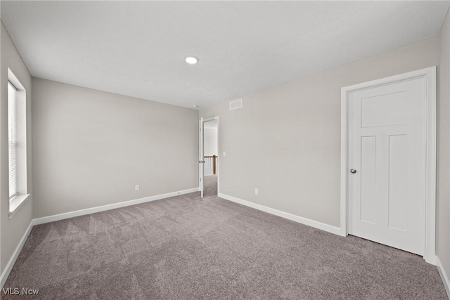 empty room with carpet, visible vents, and baseboards