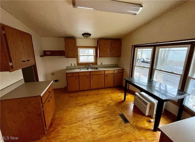 kitchen featuring brown cabinets, vaulted ceiling, visible vents, and a sink