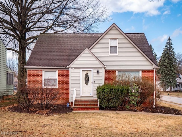 bungalow featuring entry steps, a shingled roof, a front yard, and brick siding