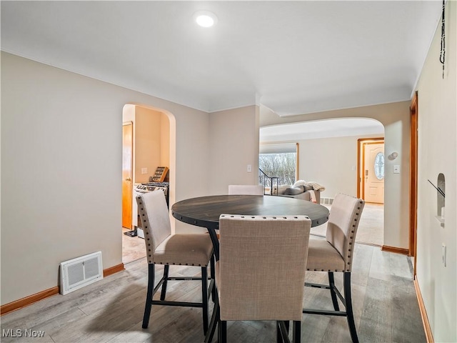 dining area featuring light wood-style floors, visible vents, arched walkways, and baseboards