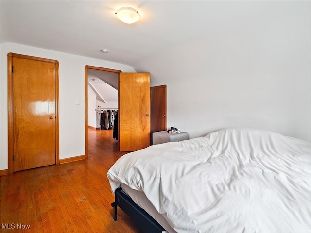 bedroom featuring lofted ceiling, baseboards, and hardwood / wood-style flooring