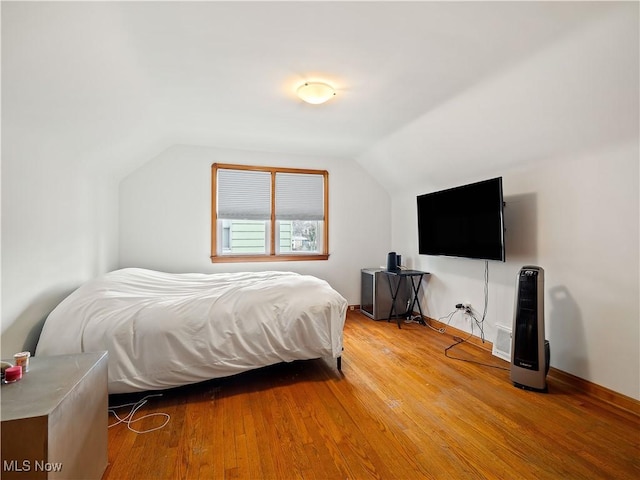 bedroom with light wood-type flooring, baseboards, and vaulted ceiling