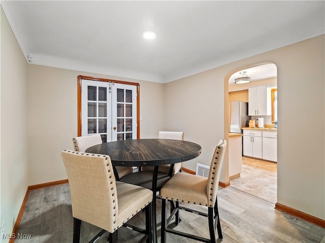 dining room featuring light wood-type flooring, arched walkways, french doors, and baseboards