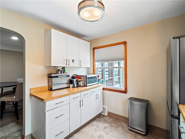 kitchen featuring visible vents, arched walkways, baseboards, freestanding refrigerator, and white cabinetry