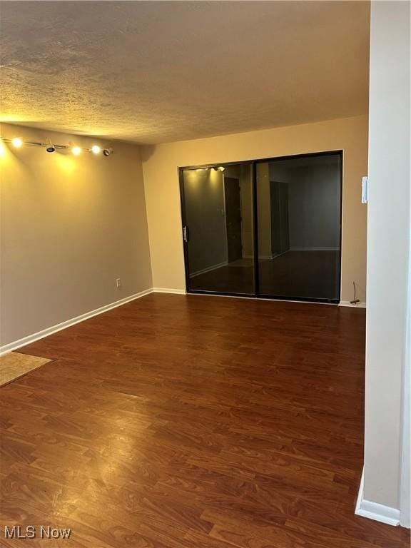 unfurnished room with a textured ceiling, baseboards, and wood finished floors